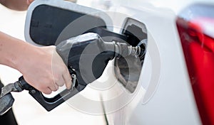 Female worker hand holding nozzle fuel fill oil into car tank at pump gas station