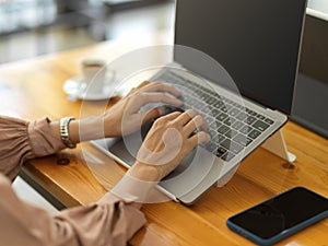 Female worker hands typing on laptop keyboard on wooden desk in cafe