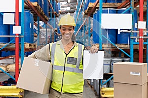 Female worker holding cardboard box and clipboard in warehouse