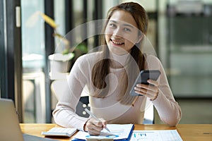 Female worker holding a smartphone and working on financial report