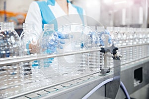 Female worker holds transparent plastic bottle background of automated dairy production line