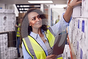 Female Worker Inside Busy Warehouse Checking Stock On Shelves Using Digital Tablet 