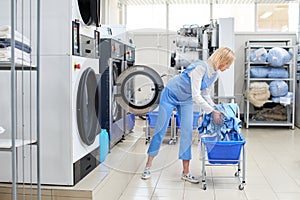 Female worker loads the Laundry clothing into the washing machine