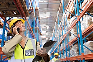 Female worker looking up while talking on mobile phone in warehouse