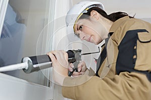 Female worker renewing silicone joint on window