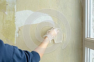 Female worker`s hand removes old wallpaper from the wall. The concept of repair, construction work