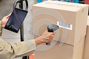 Female worker scanning package with barcode scanner while using digital tablet in warehouse