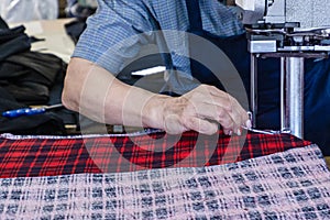 Female worker on a sewing manufacture uses electric cutting fabric machine. Textile industry, clothing production, fabric cutting