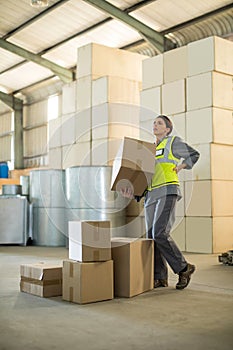 Female worker suffering from back pain while holding heavy box