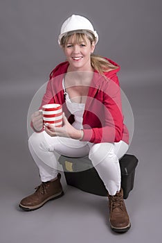 Female worker taking a tea break sitting on a toolbox