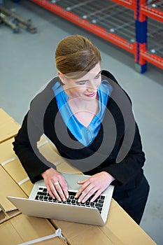 Female worker typing on laptop computer in warehouse