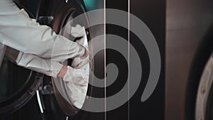 Female worker in uniform loading bed linen in washing machine at laundry