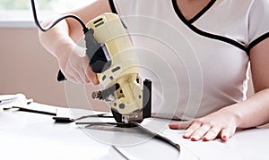 Female worker uses electric cutting fabric machine. Fabric industry production