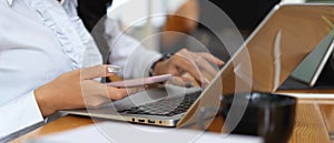 Female worker using smartphone while working with laptop on worktable