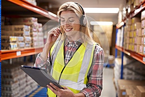 Female Worker Wearing Headset In Logistics Distribution Warehouse Using Digital Tablet