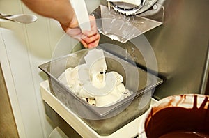 Female worker is working on ice cream maker machine. Producing vanilla ice cream with chocolate dressing.