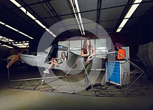 Female workers in front of plane plane fuselage and aircraft body frame in airplane hangar.