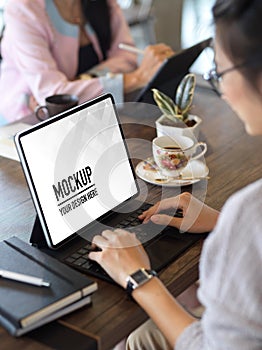 Female working with digital tablet on wooden table in cafe with coworker