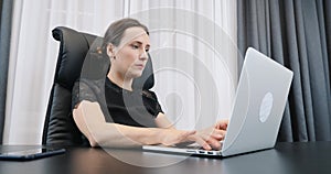 Female working on laptop in the office. Woman typing on computer keyboard. Lady boss in black dress sitting at her office desk