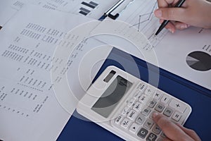 Female working in office, studying using calculator and writing something with documents and chart on table