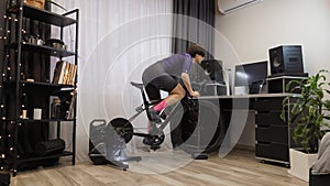 Female is working out on exercise spin bike. Woman is riding on bicycle trainer