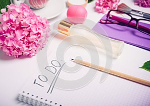 Female working place with To do list, cosmetic accessories, notebook, glasses, and wisteria flowers on the white background. Day p photo