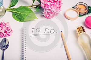 Female working place with To do list, cosmetic accessories, parfumes and wisteria flowers on the white background. Day planning. F photo
