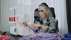 Female works on overlock in tailor`s studio. Seamstress sews fabric on sewing machine. Portrait of woman working and creating dres