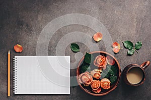 Female workspace with blank notepad, cup of coffee,ceramic bowl with flowers of coral roses and pencil. Top view, flat lay