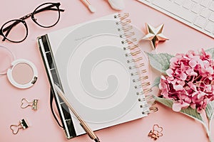Female workspace with laptop, pink hydrangea, golden accessories, pink diary on pink background