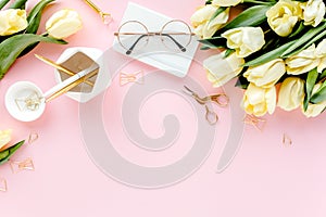 Female workspace with tulip flowers bouquet, golden accessories, diary, on pink background. Flat lay women's office desk