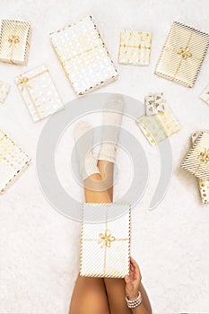 Female wrapping christmas gifts boxes for family sitting on fluffy snow-white carpet. Top view.Vertical ratio.