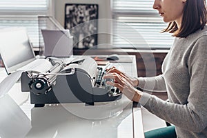 Female writer typing on a typewriter sitting in her workroom.