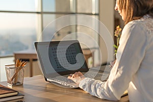 Female writer typing using laptop keyboard at her workplace in the morning. Woman writing blogs online, side view close