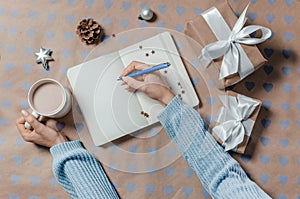 Female writing wish list in to notebook near gifts