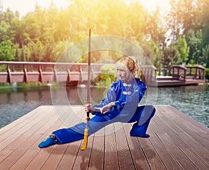 Female wushu fighter with blade against lake