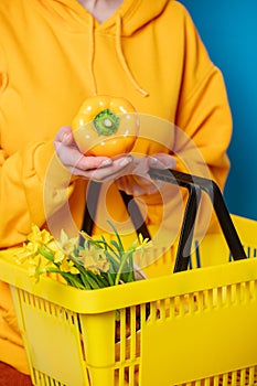Female in yellow hoodie with basket, sweet pepper and flowers