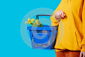 Female in yellow hoodie with blue basket and flowers on blue background