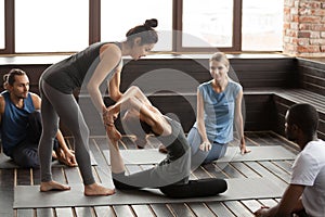 Female yoga instructor helping woman doing exercise at group tra