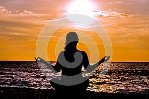 Female yoga lotos silhouette on beautiful beach during sunset.