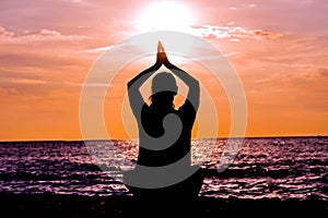 Female yoga lotos silhouette on beautiful beach during sunset.