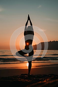 Female yoga practitioner in tree pose at beach during serene and picturesque sunset