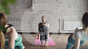 Female yoga teacher is showing upward plank pose Purvottanasana and telling about it while her students are repeating