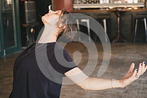 Female yogi in a backbend pose with open arms in her vinyasa flow yoga practice wearing a black t-shirt indoors