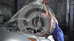 Female young auto specialist opening the hood of the car for repairing or making inspection in car service. Car service