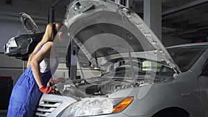 Female young auto specialist opening the hood of the car for repairing or making inspection in car service. Car service