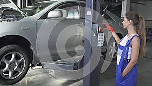 Female young automaster presses a button on a jacking lifting transport mechanism to lower the car up. Car service