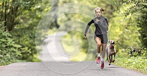 Female young sprinter runs fast up the hill followed by her dog