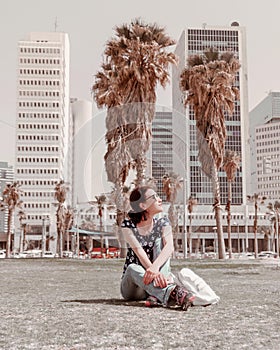 Female young tourist sits in front of business buildings in center of the city.