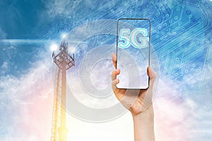 A females hand holds a cellphone against a blue sky with a 5G telecommunications tower. Concept of modern technology